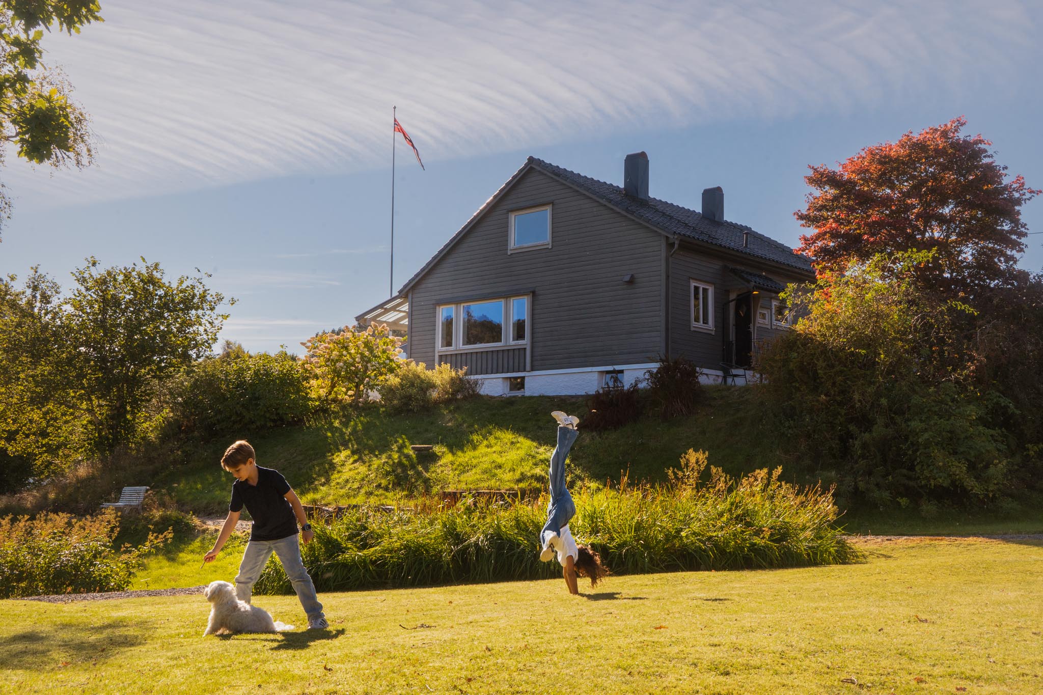 Jente og gutt sammen med en hund som leker foran et hus